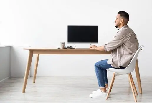 Person sitting upright at a desk with monitor and notebook